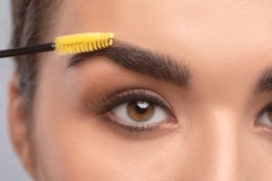 Makeup artist combs eyebrows with a brush after dyeing in a beauty salon.